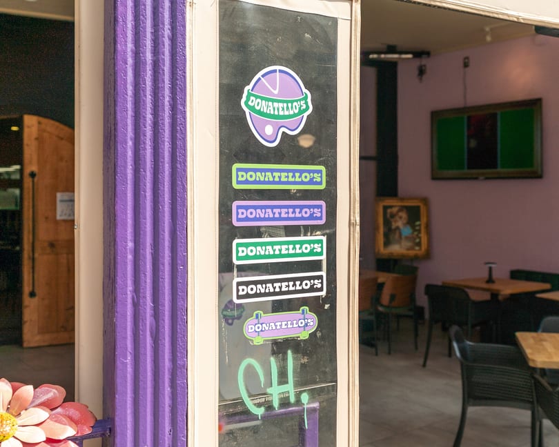 Donatello's restaurant entrance with a purple column and multiple colorful Donatello's stickers on the glass door.