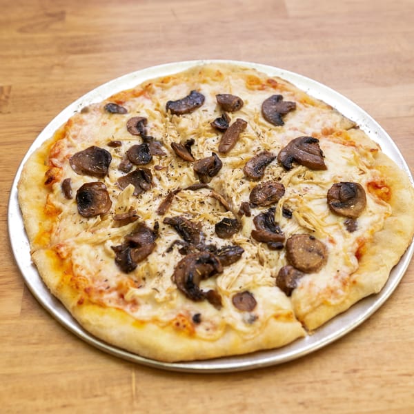 A whole mushroom and chicken pizza on a metal pan, resting on a wooden table.