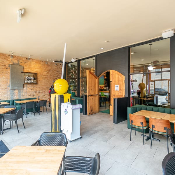 Restaurant interior with brick walls, green booth seating, wooden tables, and a yellow lollipop sculpture.