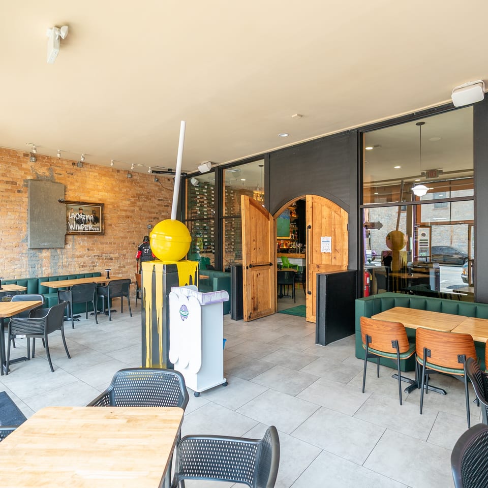 Restaurant interior with brick walls, green booth seating, wooden tables, and a yellow lollipop sculpture.