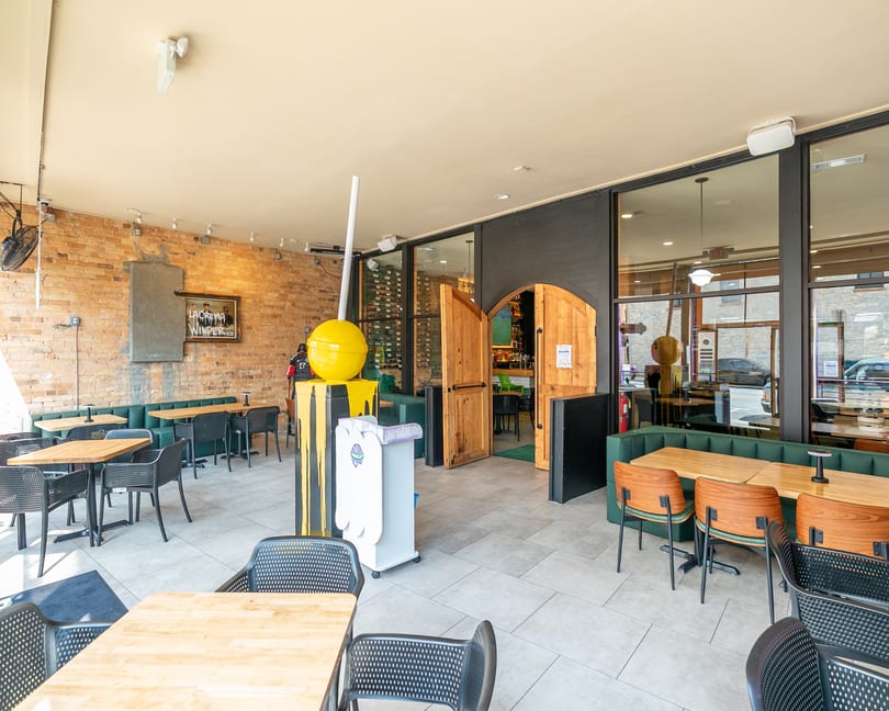 Restaurant interior with brick walls, green booth seating, wooden tables, and a yellow lollipop sculpture.
