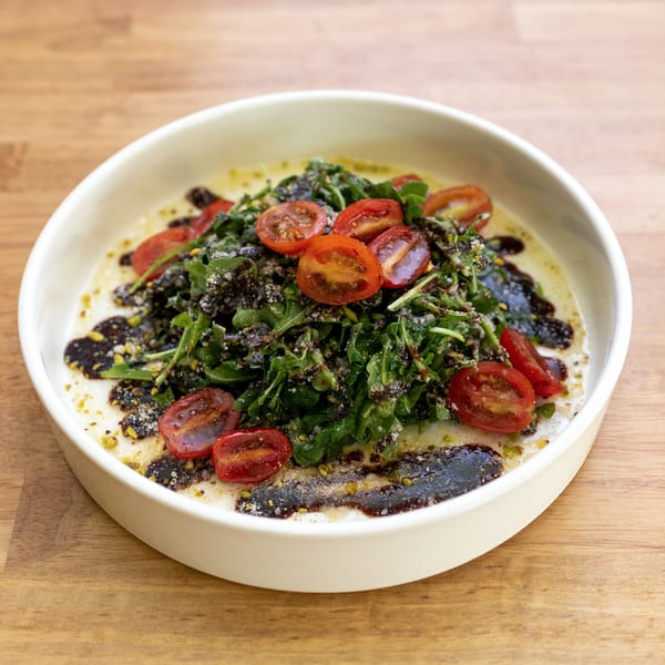 Arugula salad with halved cherry tomatoes, dark dressing, and cheese in a white bowl.