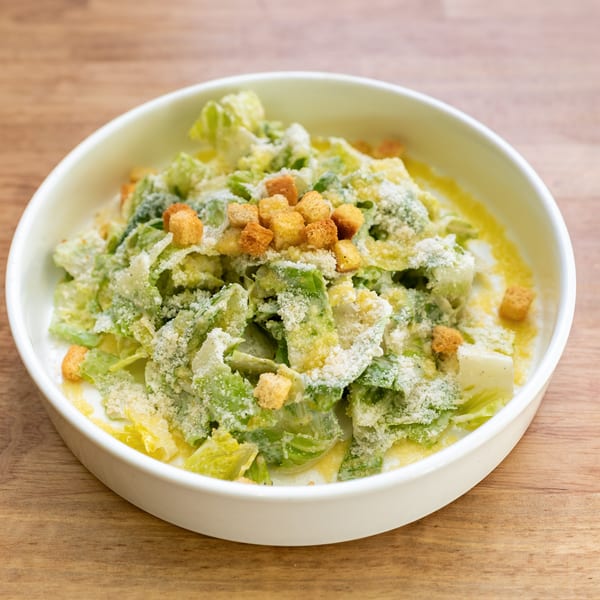 A white bowl filled with Caesar salad, topped with croutons and grated Parmesan cheese.
