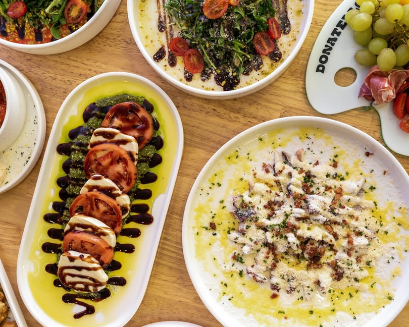 Overhead view of various Italian dishes, including Caprese salad, pasta, and a charcuterie board.