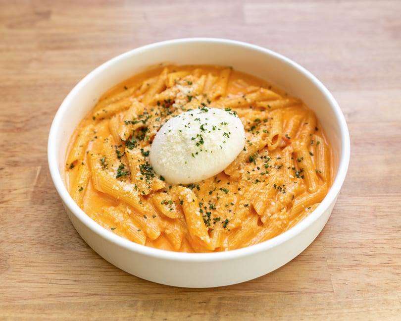 Penne pasta in a creamy orange sauce, topped with a dollop of ricotta cheese and parsley.