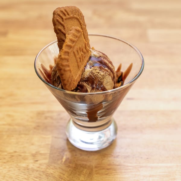 Scoop of ice cream with chocolate drizzle and two Biscoff cookies in a glass.