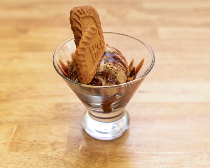 Scoop of ice cream with chocolate drizzle and two Biscoff cookies in a glass.