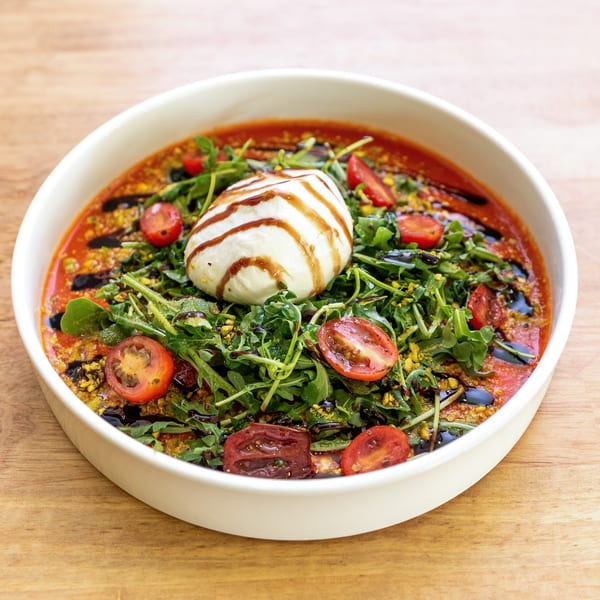 Burrata cheese with arugula, cherry tomatoes, and balsamic glaze in a white bowl.
