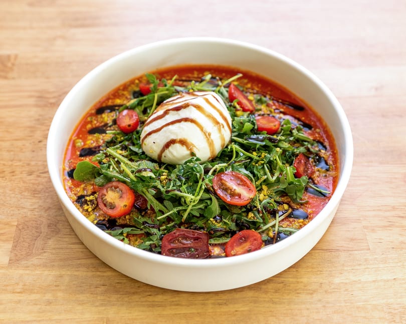 Burrata cheese with arugula, cherry tomatoes, and balsamic glaze in a white bowl.