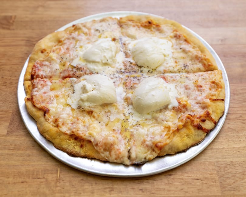 A whole cheese pizza with four dollops of fresh mozzarella and herbs on a metal tray.